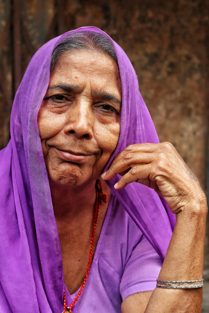Close-up portrait of a smiling elderly woman in vibrant purple traditional clothing, exuding warmth and wisdom.